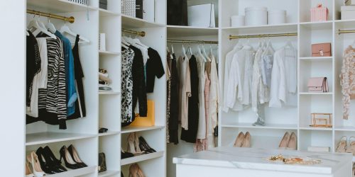 A stylish walk-in closet featuring luxury clothing, shoes, and accessories, with elegant shelving and chandeliers.
