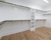 Modern empty walk-in closet with wooden flooring and white shelving.