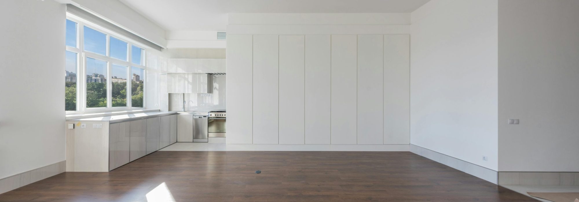 Bright and spacious modern kitchen interior featuring wooden floors and white cabinetry.
